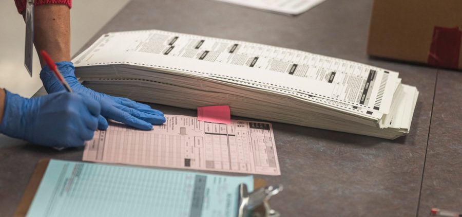 A poll worker wearing gloves handles a stack of ballots