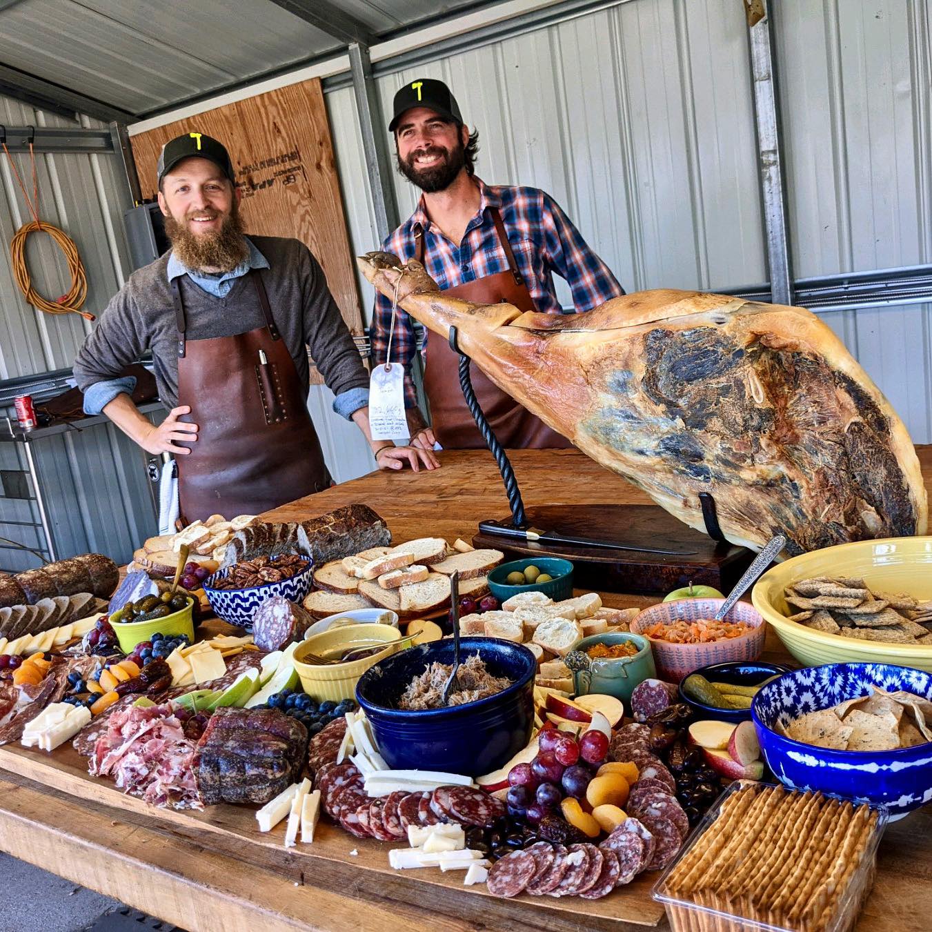 An image of two people in front of a spread of various types of meats and crackers.