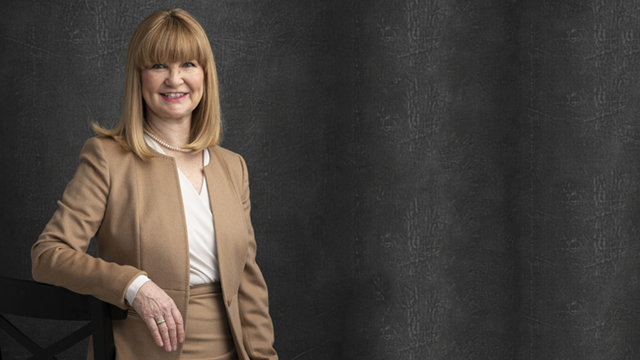 A promotional image of Miranda Esmonde-White, posed against a plain dark background in a tan suit.