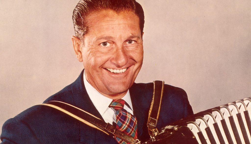 A promotional image of Lawrence Welk. He is smiling and holding an accordian against a plain white background.