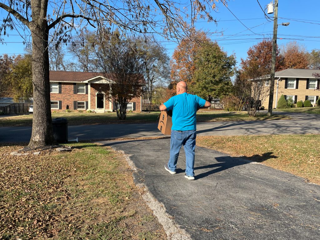 Rick Lucas walks toward the end of his driveway while carrying an Amazon delivery box.