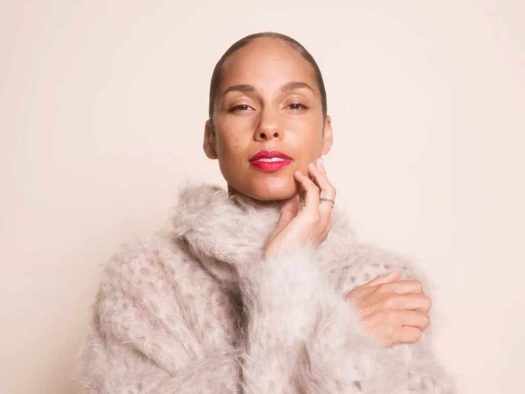 A promotional image of Alicia Keys. She is wearing a white fuzzy sweater and is posed against a beige background.