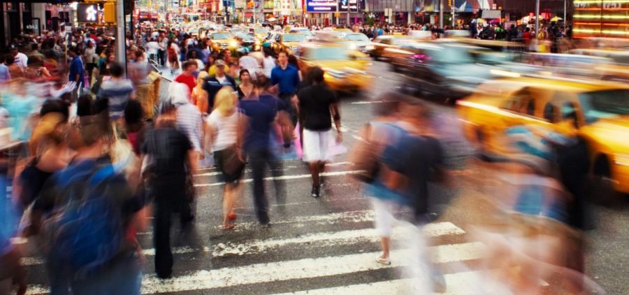 People walk in a cross walk in a busy city. They are blurred because of how fast they are walking.