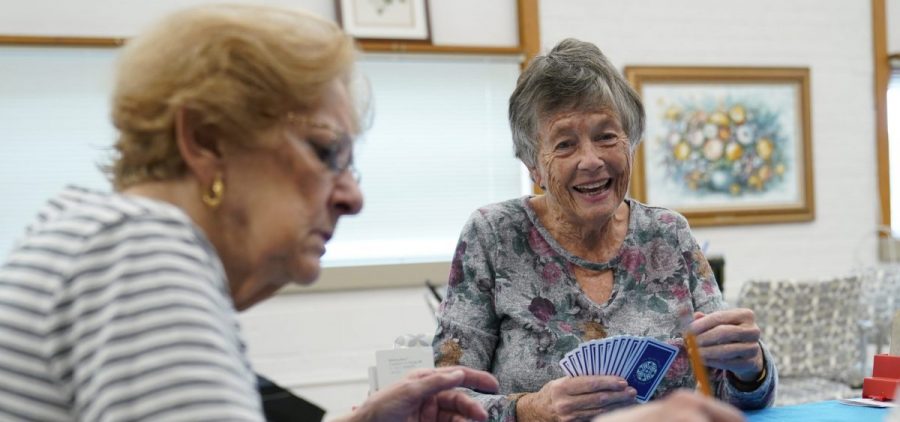 Two women play a card game together. One laughs while the other looks deep in concentration.