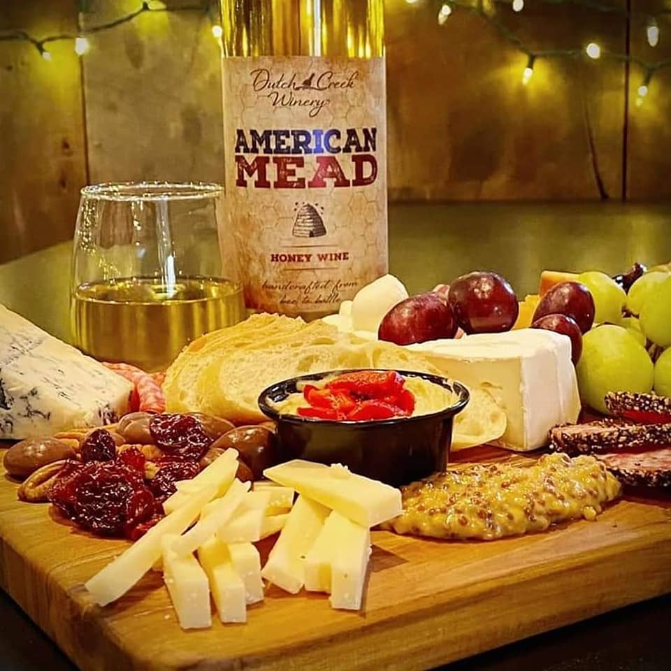 An image of a charcuterie tray with meat and cheese, as well as a bottle of mead.