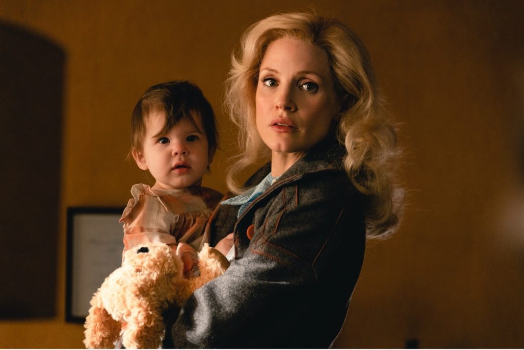 Tammy Wynette, portrayed here by Jessica Chastain, moved to Nashville as a single mother of 3 daughters after splitting with her first husband. Chastain has a baby in her arms and looks to the viewer.