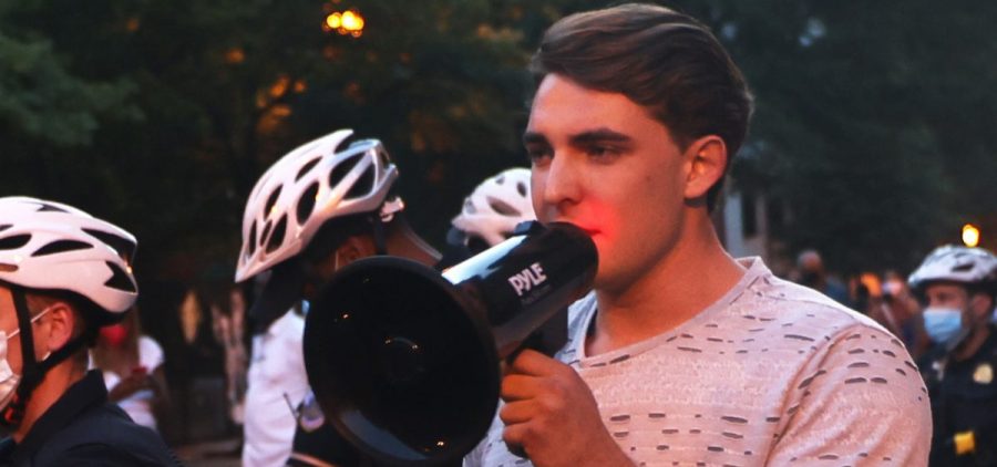 Jacob Wohl, pictured here surrounded by police officers at a 2020 protest in Washington D.C. holds a bullhorn