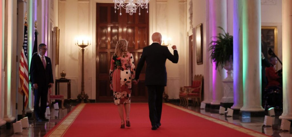 President Biden and first lady Jill Biden walk through the Cross Hall of the White House lit with rainbow colors