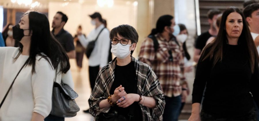 A group of people stand in a public indoor space. Some wear facemasks.