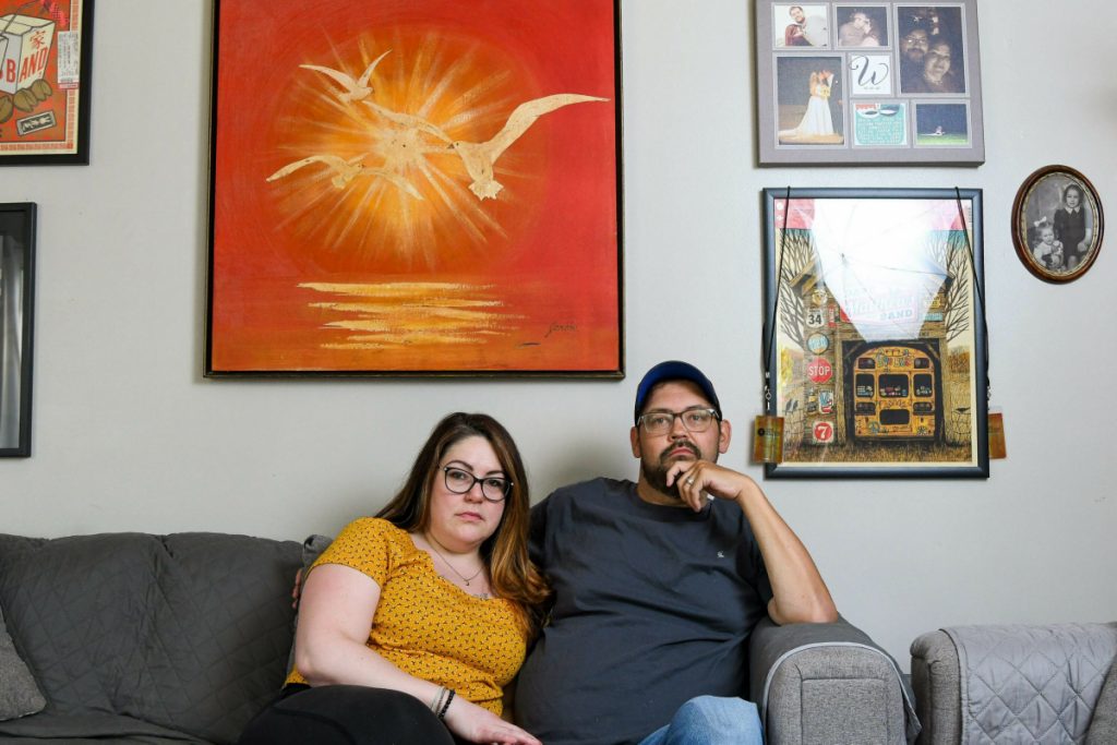 Nick and Elizabeth Woodruff pose for a portrait in their home. They are sitting on a gray couch.