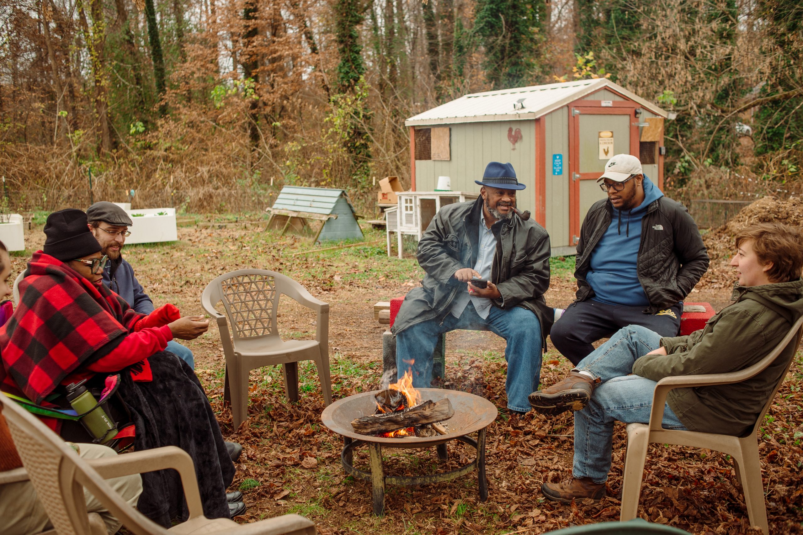 A group of people sit around a fire pit and talk.