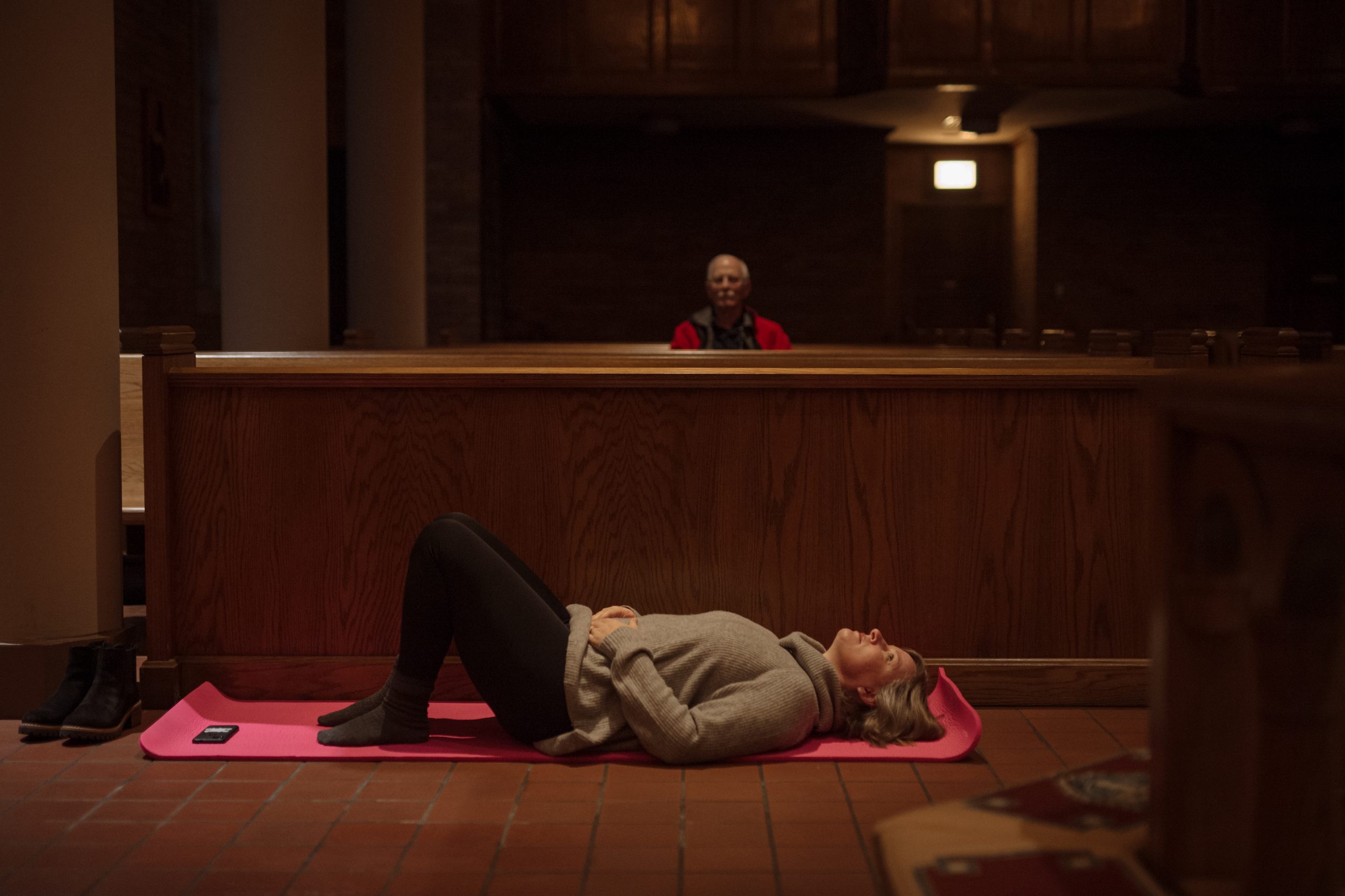 A woman lies on a yoga mat behind a church pew.