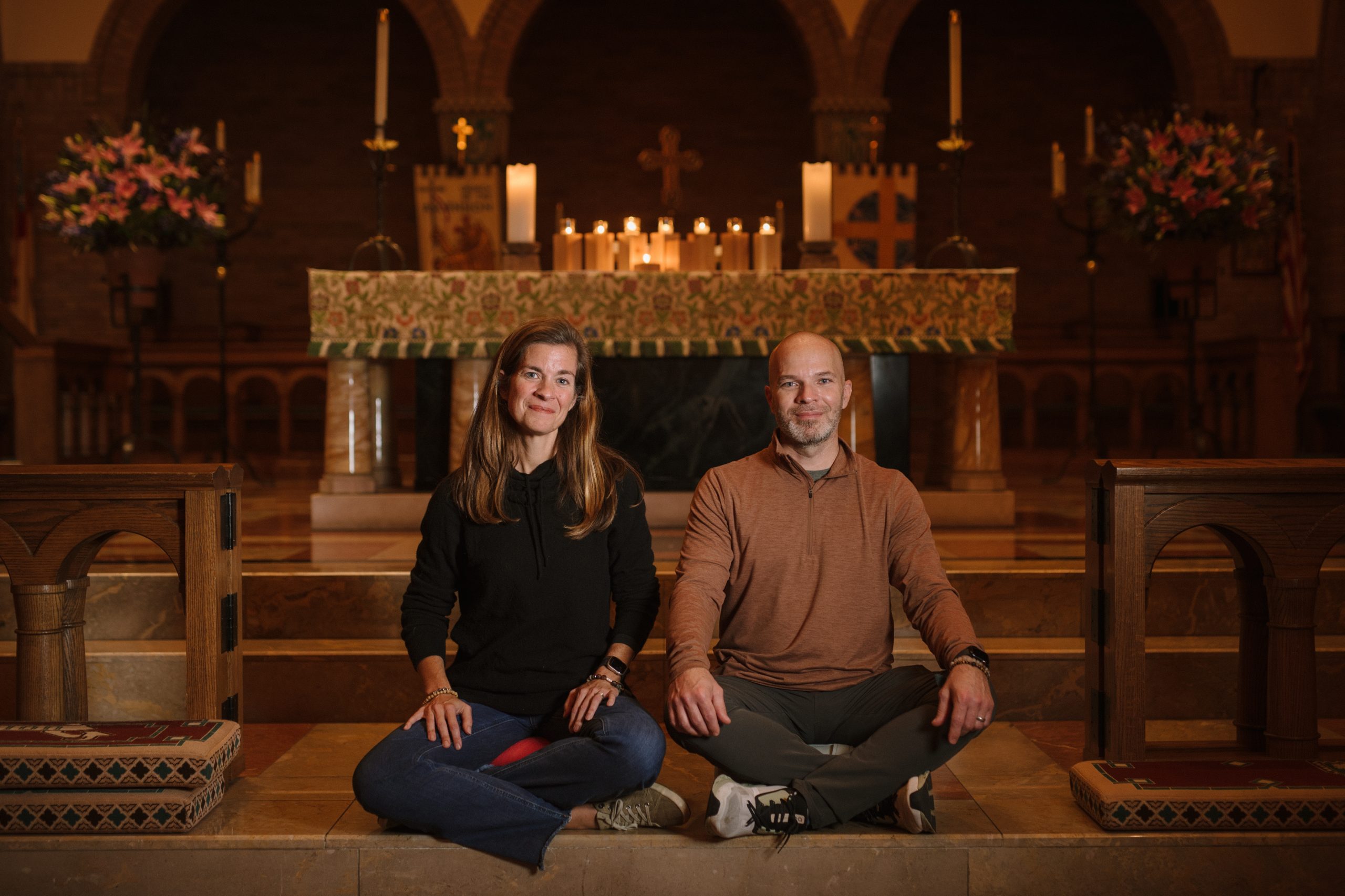 A man and woman sit cross-legged in front of a candlelit church altar.