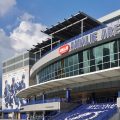 The outside of Amalie Arena in Tampa Florida on a sunny day. You can see glass windows on the upper part of the wall and the Amalie Arena Logo in giant blue letters.