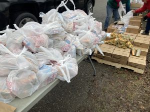 Plastic bags holding blocks of cheese sit on a foldout table on a paved road. Cardboard boxes with additional blocks of cheese are nearby.