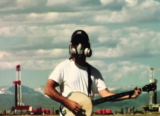 An image of someone wearing a gas mask and holding a banjo against a blue cloudy sky.