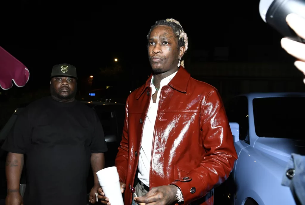 Rapper Young Thug wearing a red leather jacket with a packet of paper in his hands.