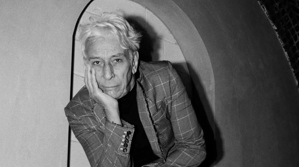 A promotional image of musician John Cale. It is black and white and John Cale is resting his head on one hand.