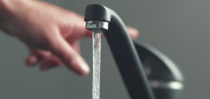 A hand reaches up to a water faucet as water pours out