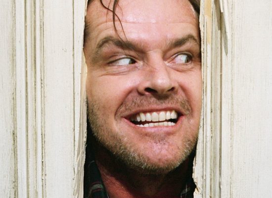 A still from "The Shining" featuring Jack Nicholson peering out from the hole he cut in the door.