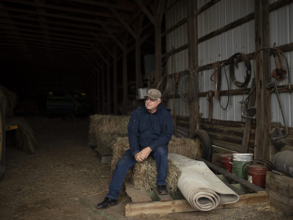 A man sits in a barn on a hay bale.
