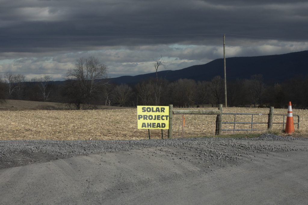 A sign in front of a large field reads "Solar Project Ahead."