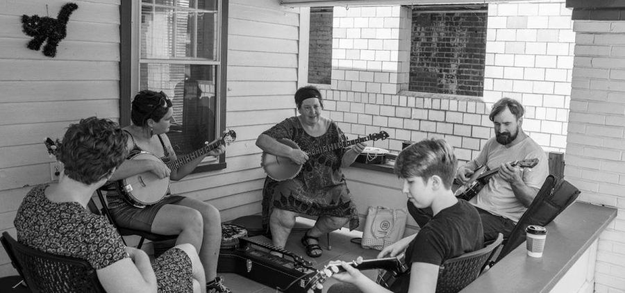 A black and white photo of a group of people engaged in a traditional stringed instrument lesson on a porch.