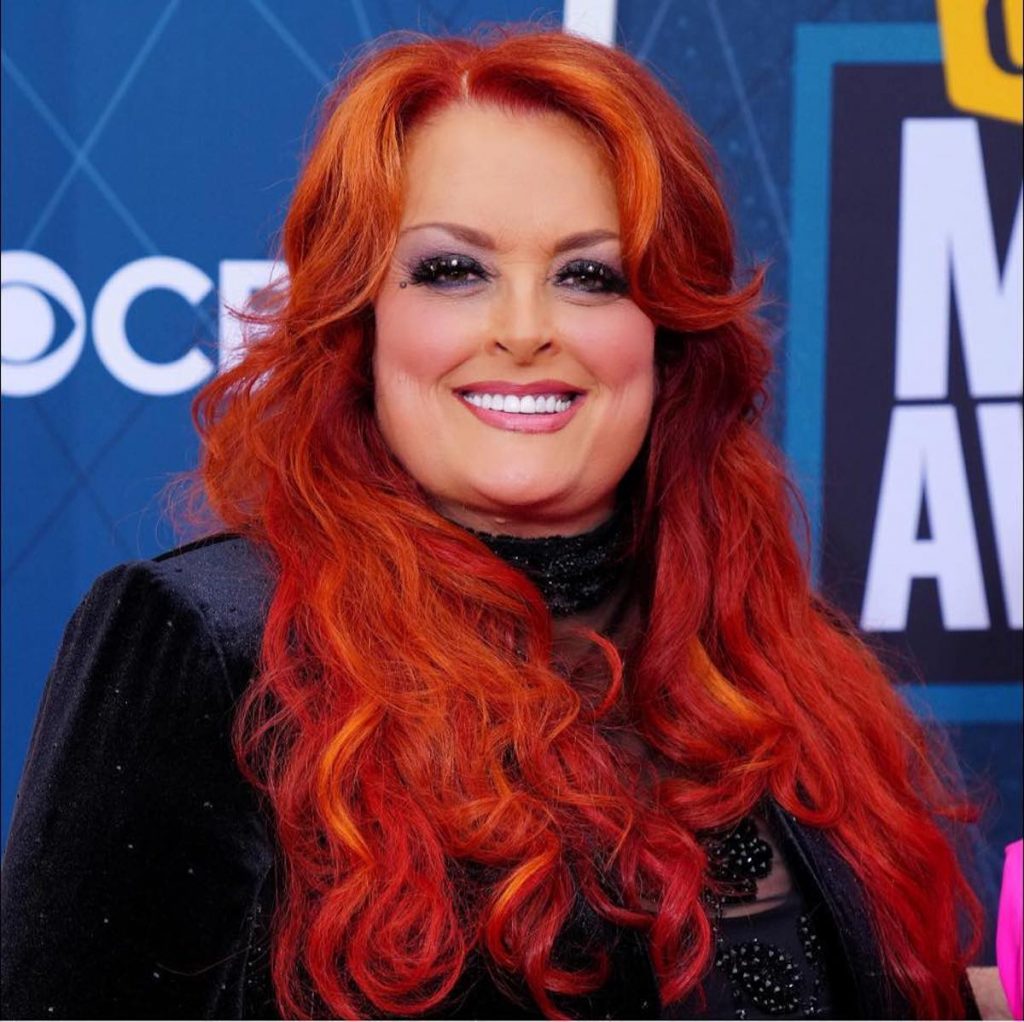 A picture of Wynonna Judd, who has red hair and is posed against a blue background. 