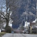A man takes photos as a black plume rises over East Palestine, Ohio, as a result of a controlled detonation of a portion of the derailed Norfolk Southern train.