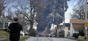 A man takes photos as a black plume rises over East Palestine, Ohio, as a result of a controlled detonation of a portion of the derailed Norfolk Southern train.