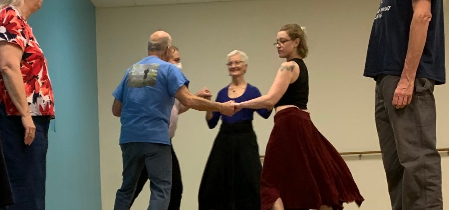 An image of people dancing, three of them are wearing skirts, and two of them are wearing pants.