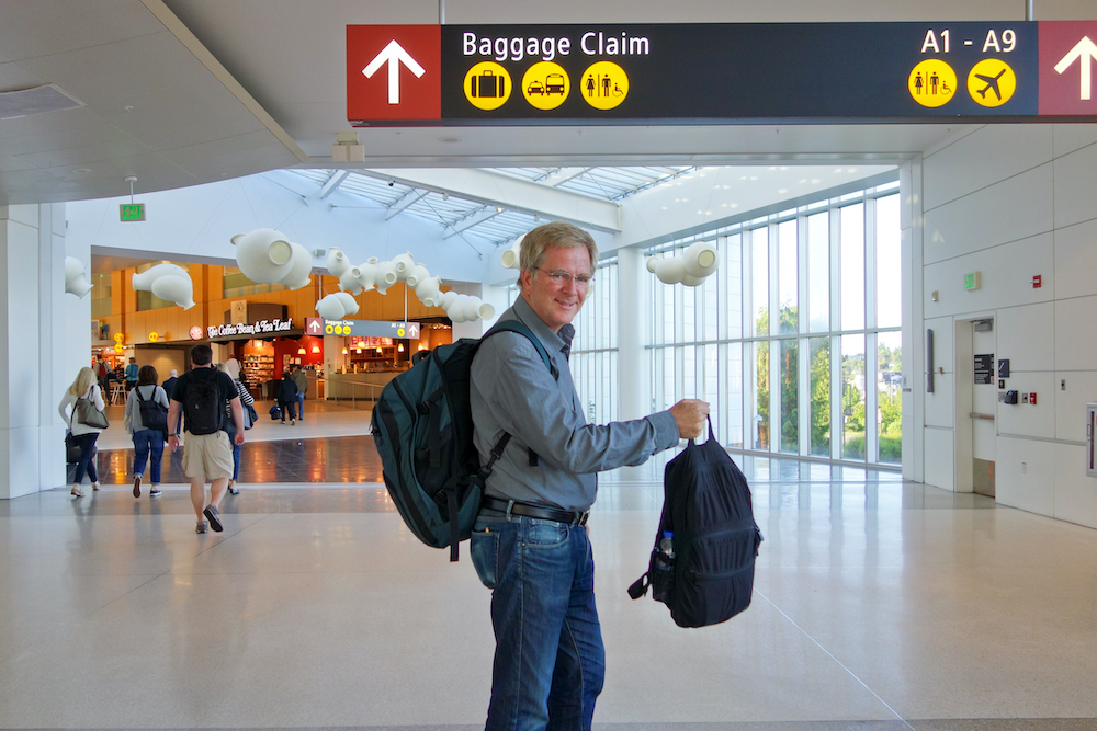An image of Rick Steves in an airport, with two backpacks.