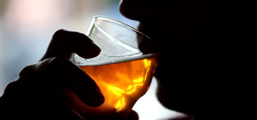 A silhouette of a person drinking an amber-colored alcoholic beverage from a glass.