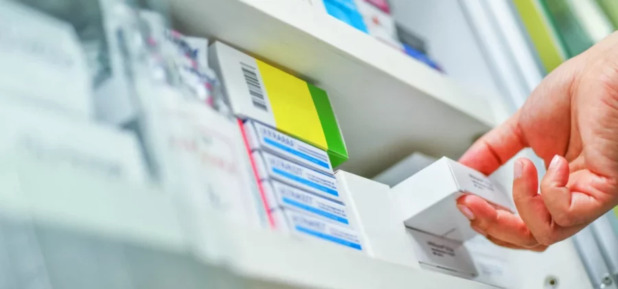The hand of a pharmacist pulls a medication down from a shelf
