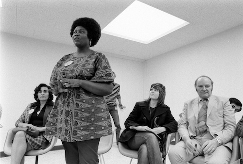 Ruby Duncan standing and addressing group, with Jane Fonda seated and listening