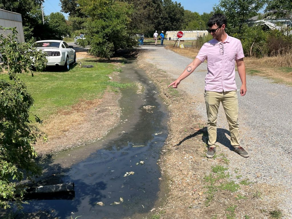 Payden Donahoe of Communities Unlimited points to sewage draining out of a pipe next to a road in Darling, Miss., on Sept. 20, 2022.