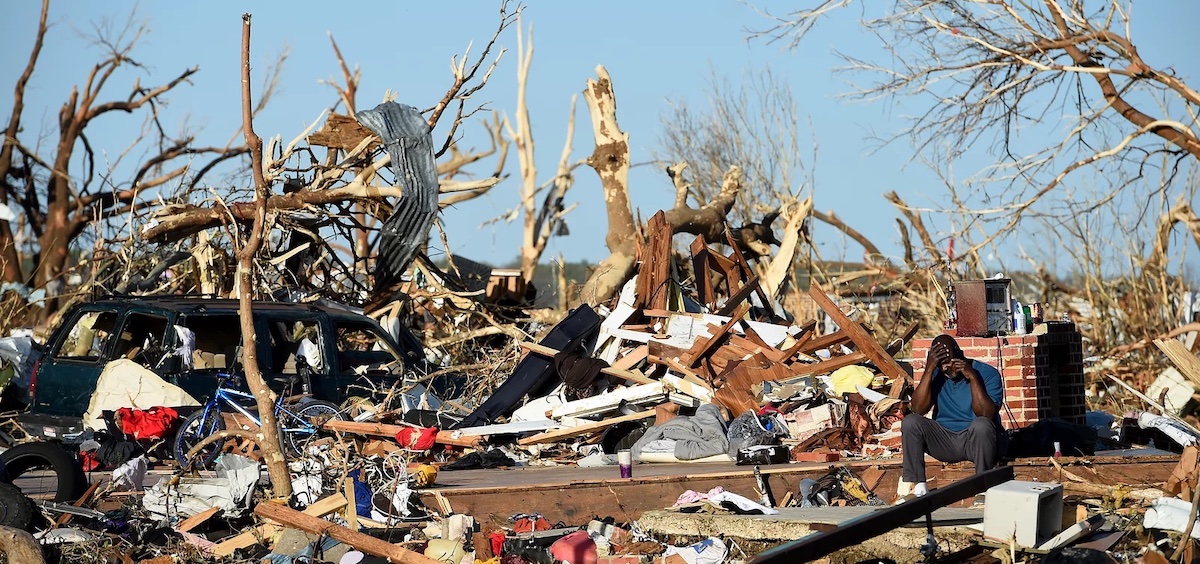 A man sits among the wreckage caused by a series of powerful storms and at least one tornado on March 25, 2023 in Rolling Fork, Mississippi.