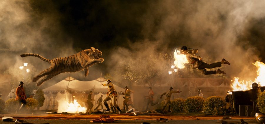 A still from the film "RRR." The still depicts a tiger and a man jumping into the air towards each other against a smoky, dark background.