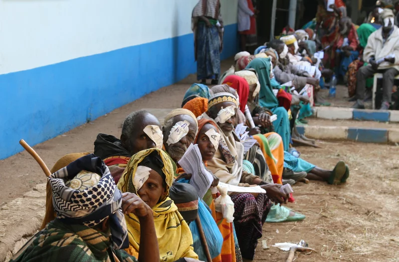 Patients in Ethiopia sit on the curb after receiving cataract surgery. They have bandages over their eyes. 