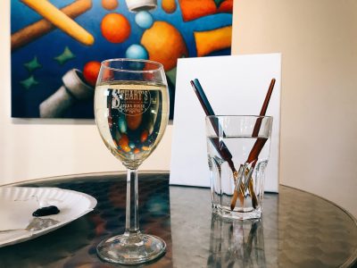 An image of a glass of wine next to a glass with pencils in it.