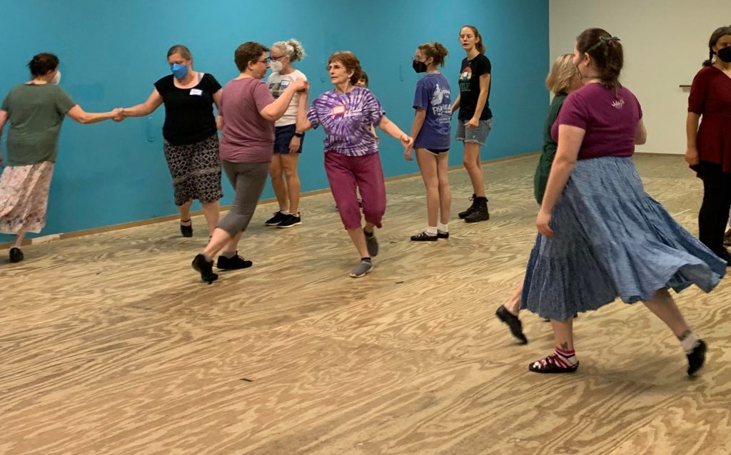 An image of people doing a Scottish dance together in a dance recital space with a mirror on the back wall.