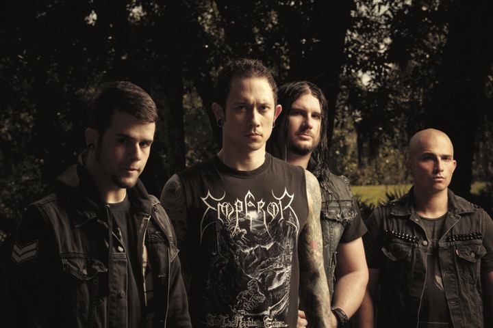 A promotional image of the band Trivium. All four members are outside and are wearing black clothes.