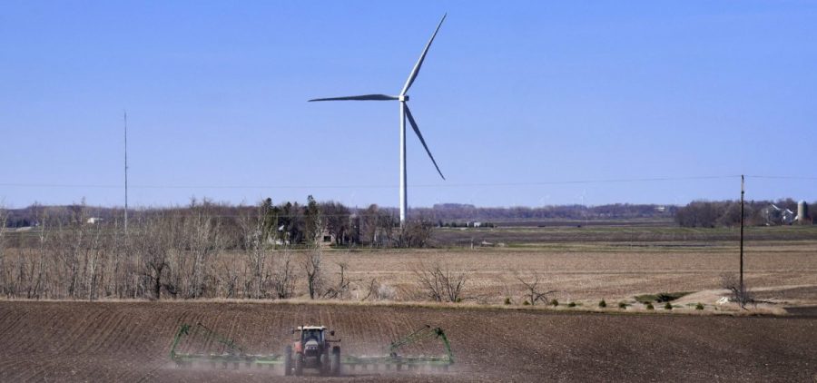 A tractor plows a field of corn with a wind turbine in the background.