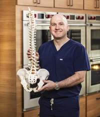 Dr. Griffin Baum poses for a portrait holding a model spine