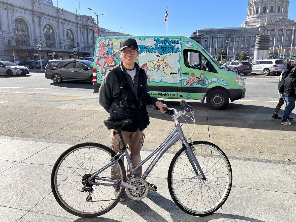 A man stands smiling with his bike on a San Francisco sidewalk.