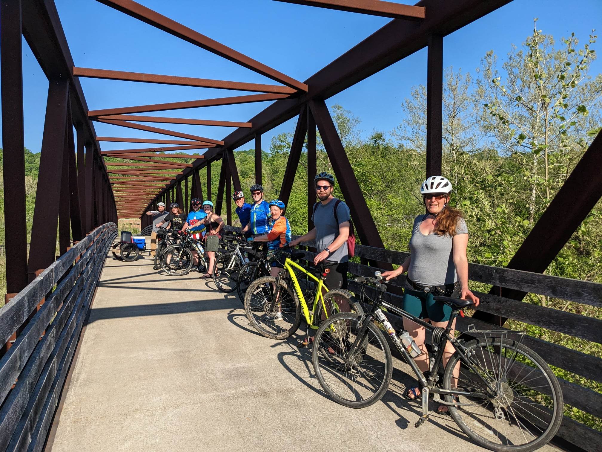 An image of people with bike helmets and bikes, pictured on an outdoor bridge.