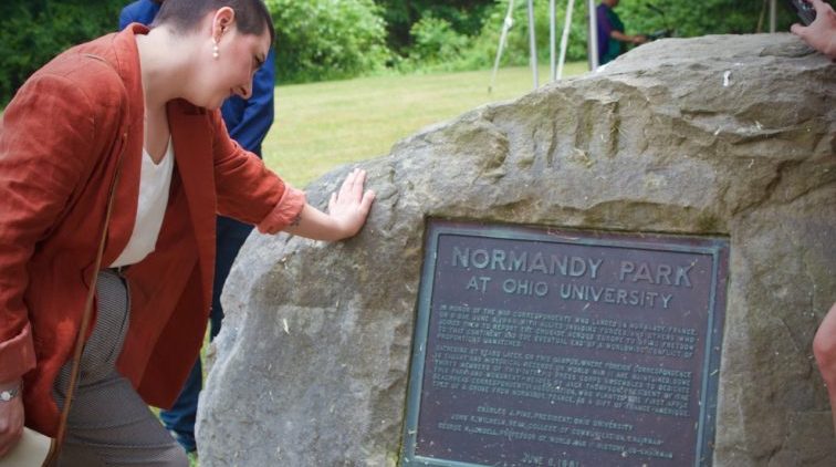 A person stands in front of a historical marker, reading the inscription at Ohio University’s event honoring war correspondents who covered the historic D-Day invasion and World War II.