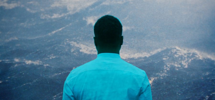 back of black man staring forward at mountain lands
