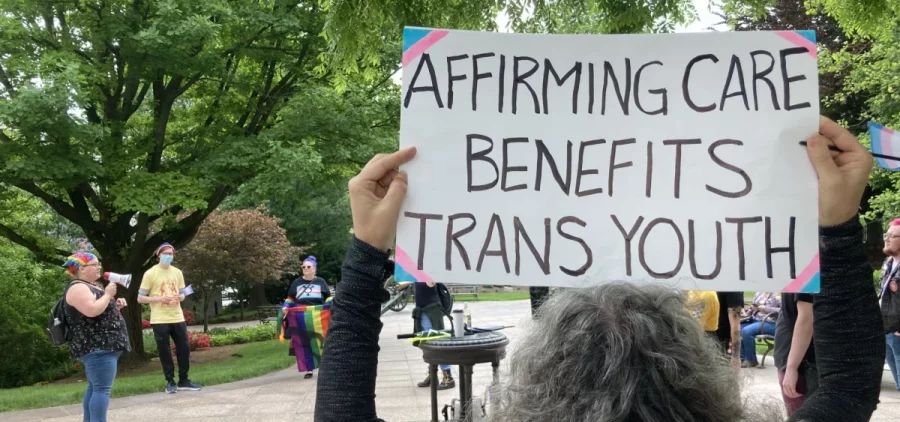 A woman holds a sign that reads Affirming Care Benefits Trans Youth at a protest