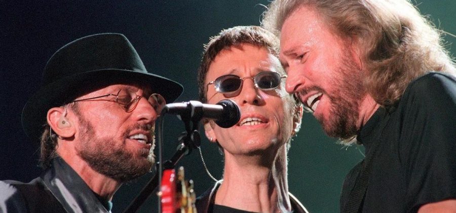 The BEE GEES surrounding and singing into a single microphone
